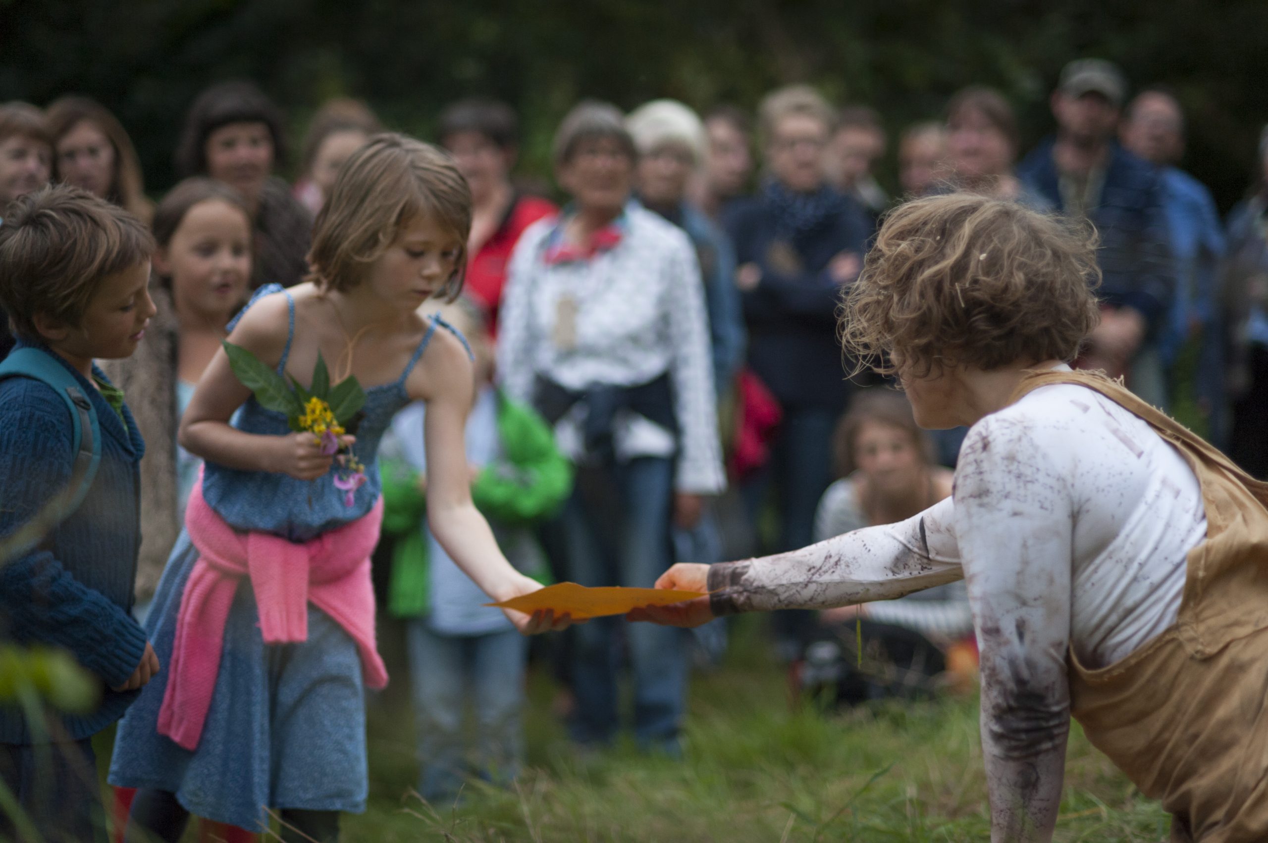 A young audience member, holding a bunch of wild flowers, is handed a piece of paper by the Wolf Girl Alice.