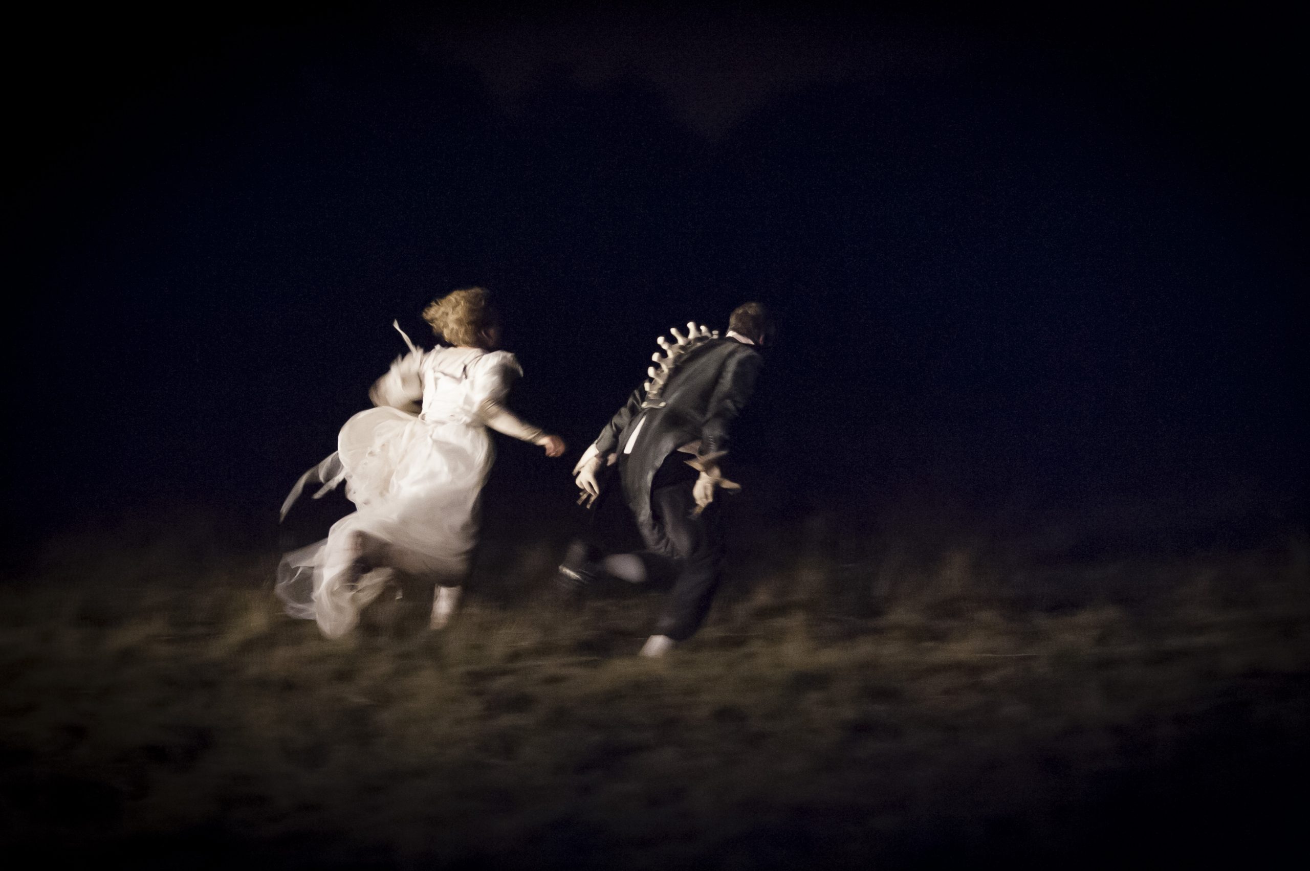 The Wolf Girl Alice, wearing a wedding dress, and The Duke in a tailcoat, an exposed animalistic spine protruding from it, run off into the darkness.