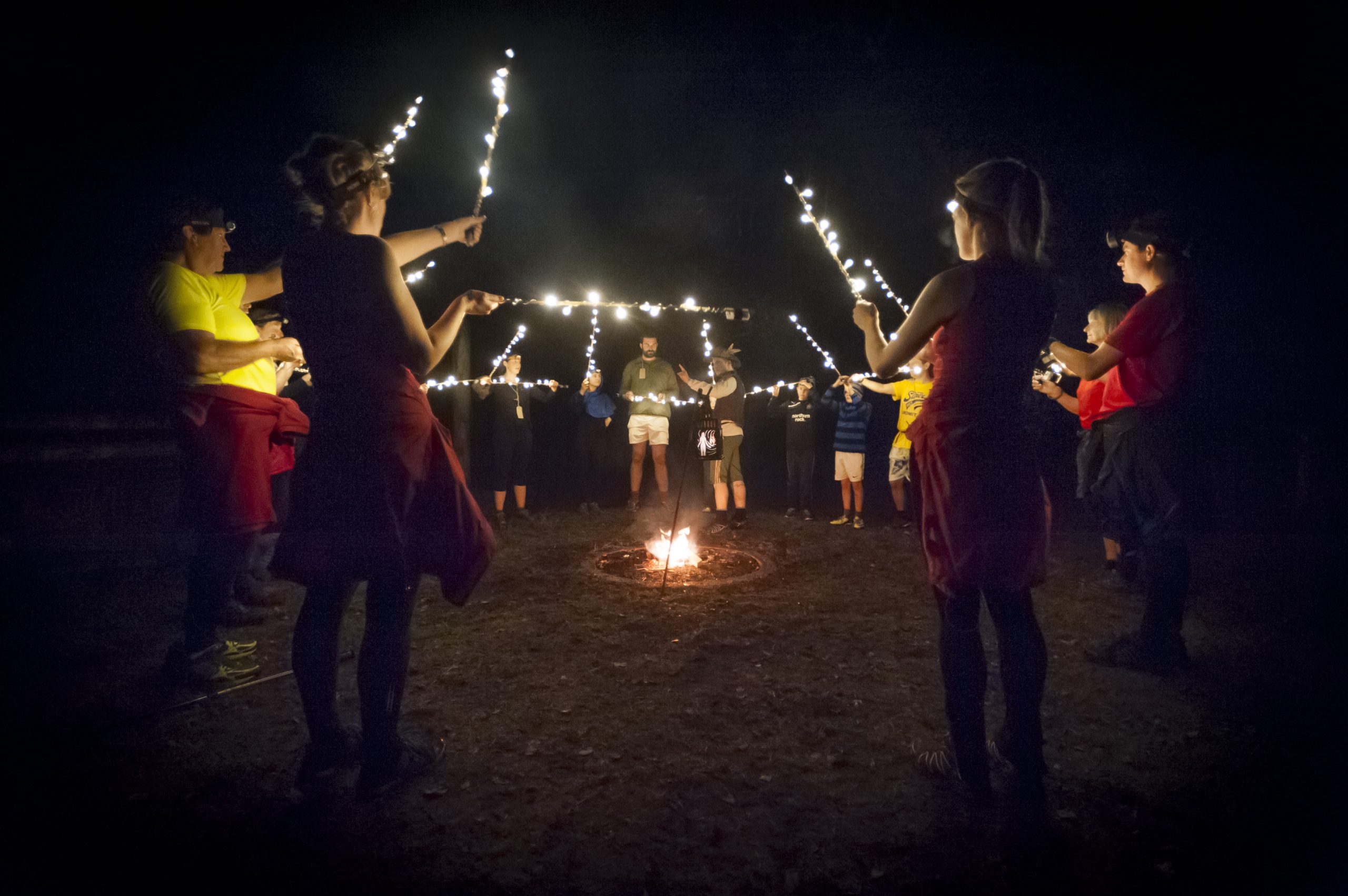 The audience stood in a circle around a fire, hold up bamboo canes covered in fairy lights, as The Huntsman tells them a story.