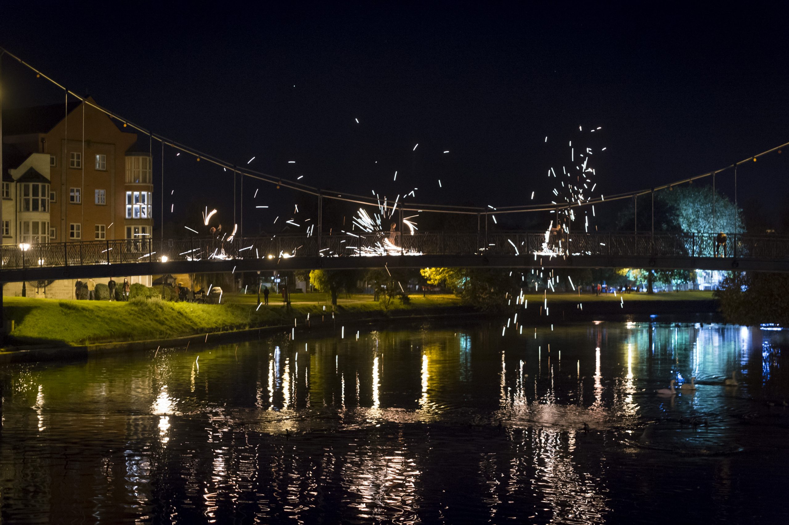 On a bridge over Exeter canal, fire spinners perform, sparks flying off into the night sky.