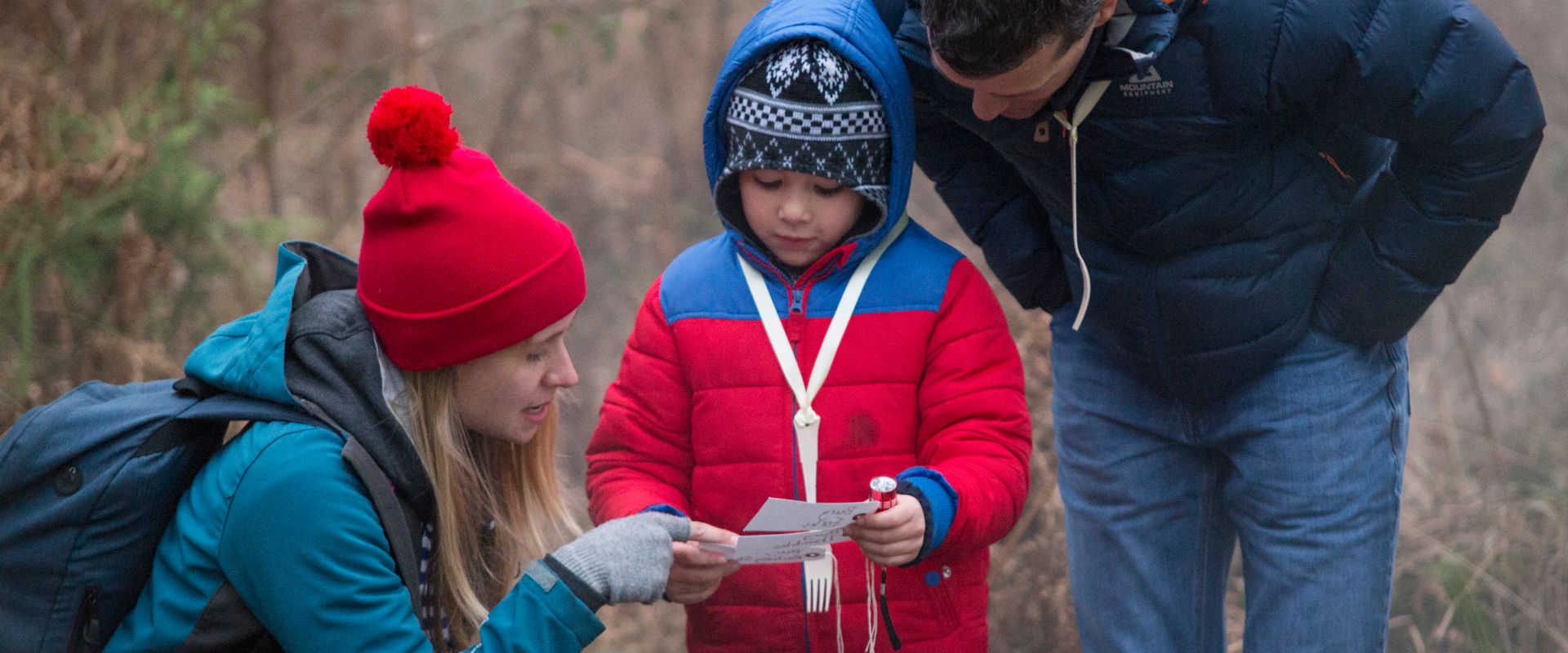 Red, bobble-hatted crew member and a child, read luggage labels together.