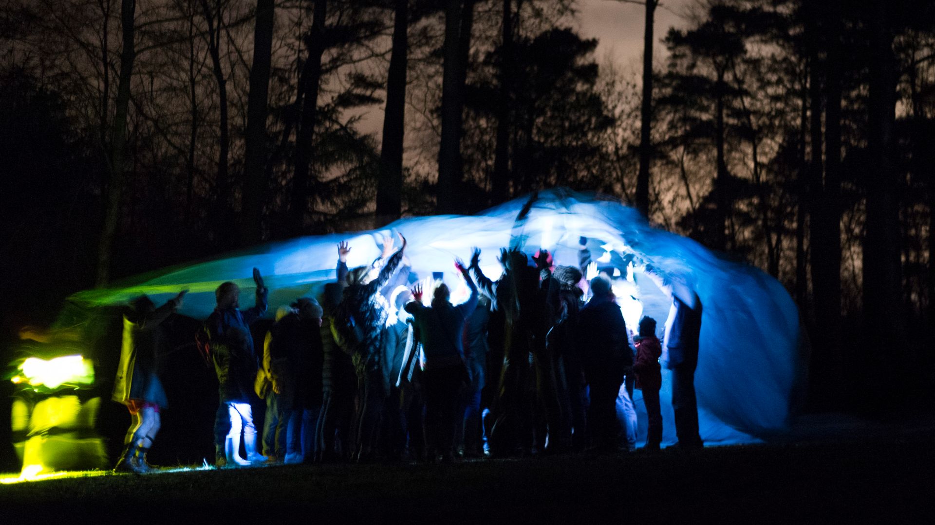 An illuminated blue parachute covering the audience in the forest at night.