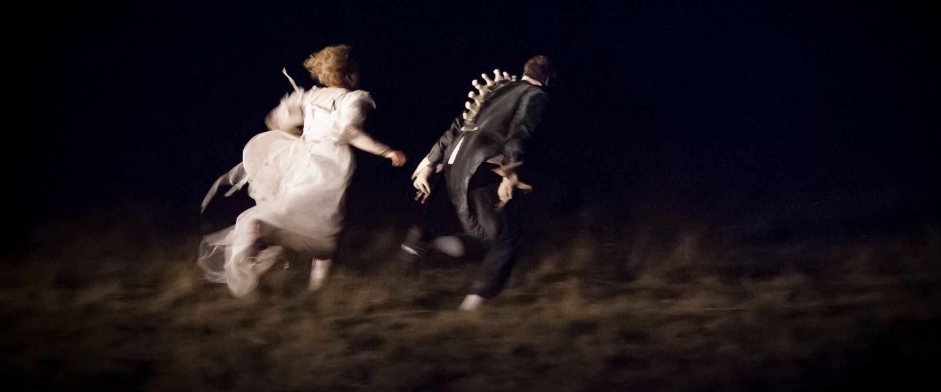 The Wolf Girl Alice, wearing a wedding dress, and The Duke in a tailcoat, an exposed animalistic spine protruding from it, run off into the darkness.