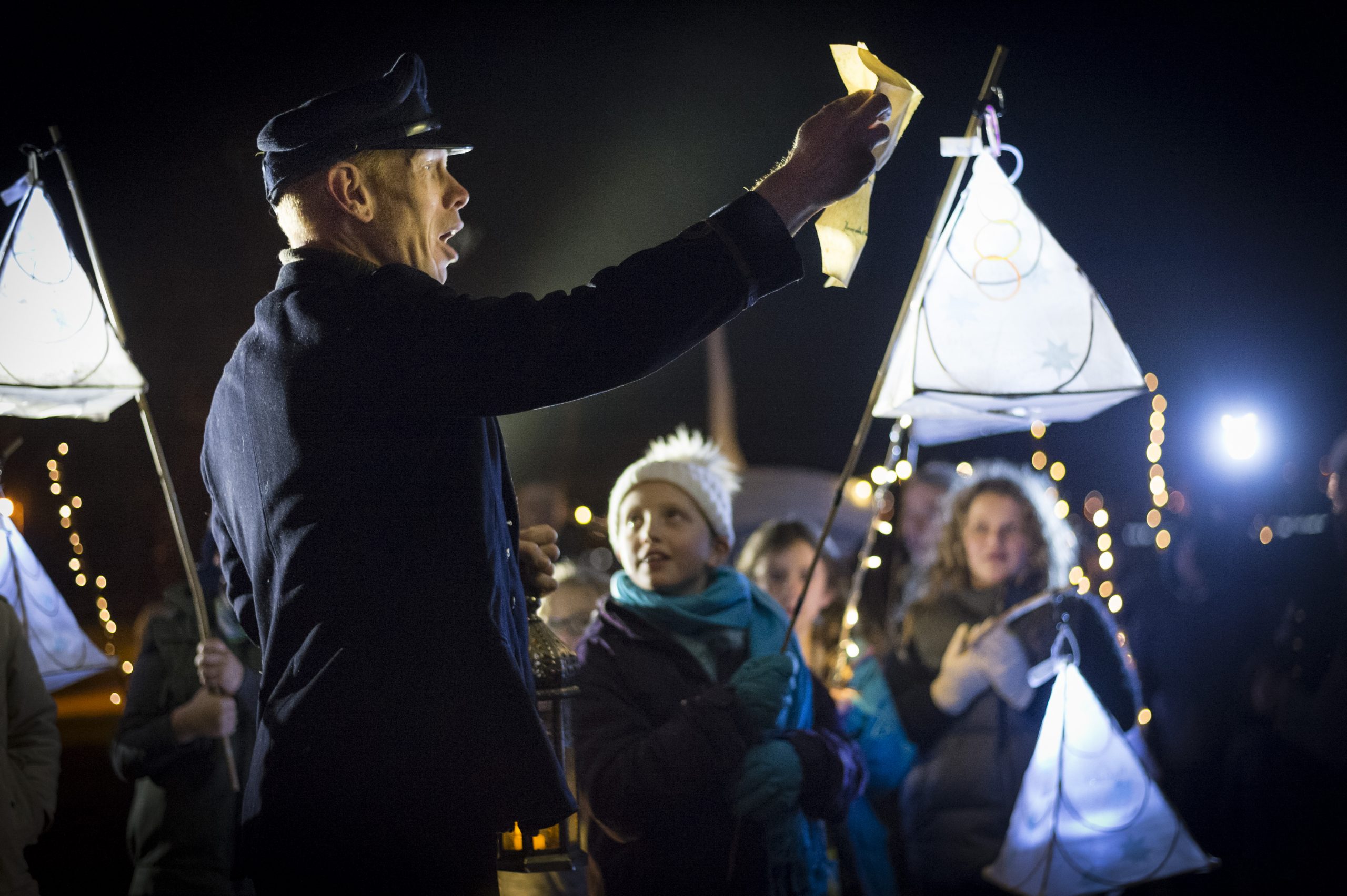 The Bridge Keeper holds up a letter and reads it to the gathered audience.