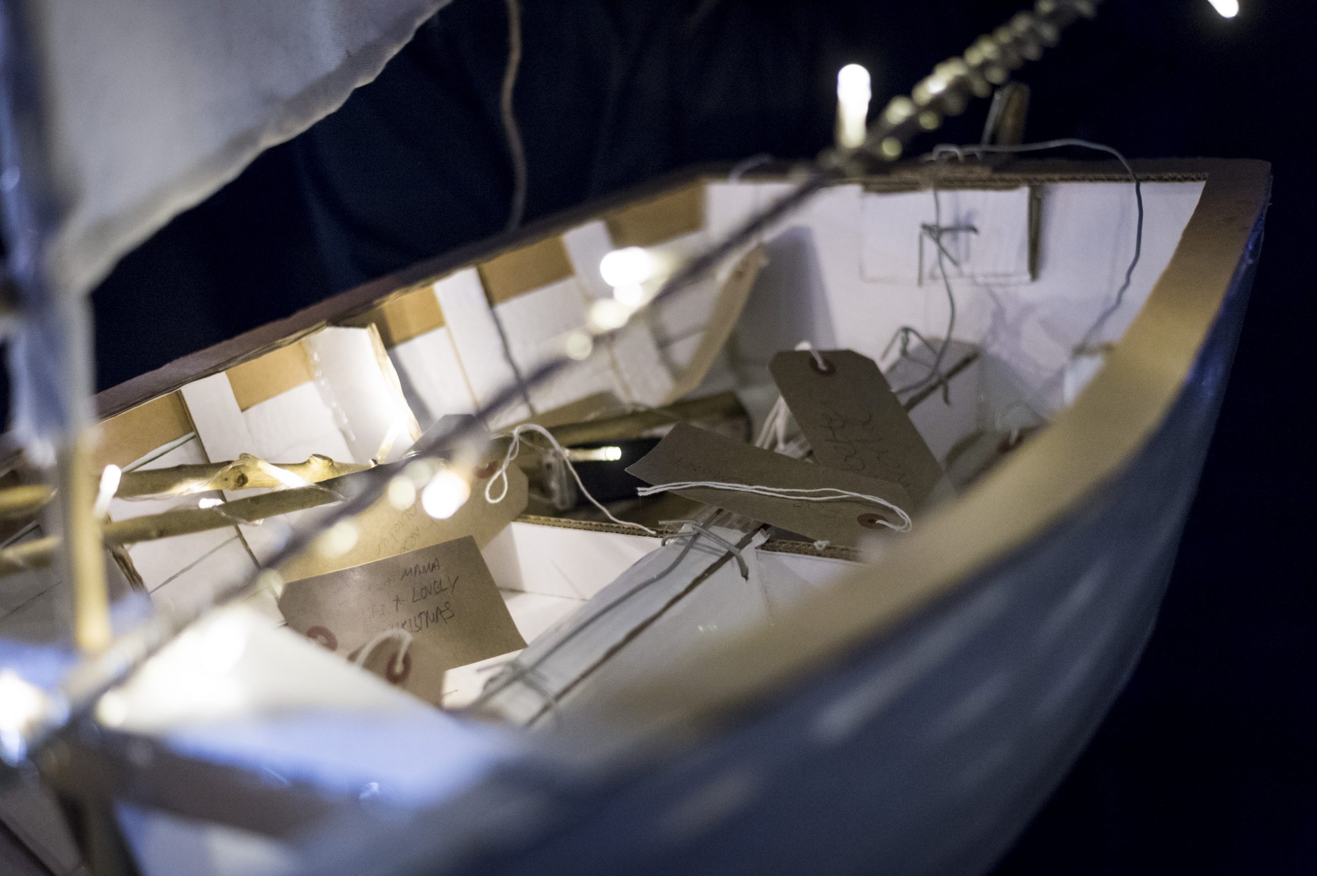 A close up of luggage labels, with personal messages written on them, inside of a small cardboard boat.