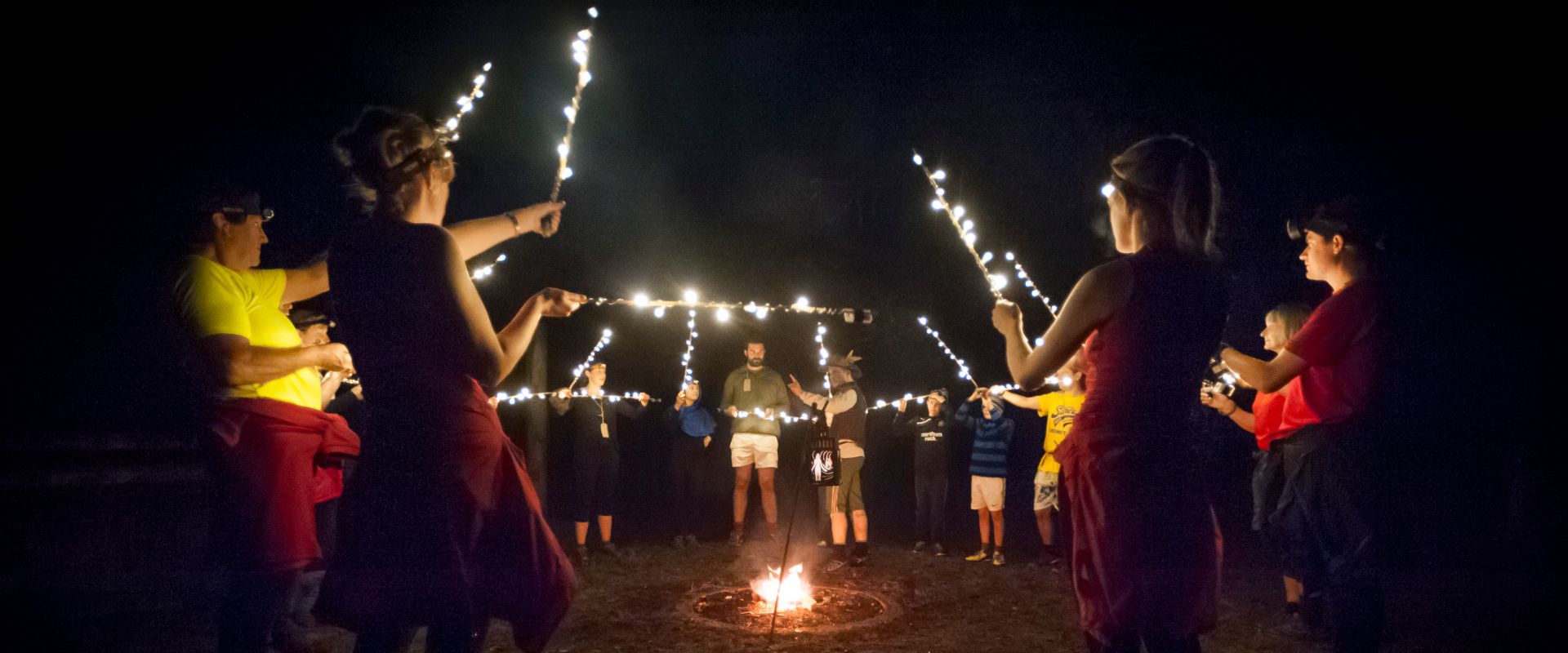 The audience stood in a circle around a fire, hold up bamboo canes covered in fairy lights, as The Huntsman tells them a story.