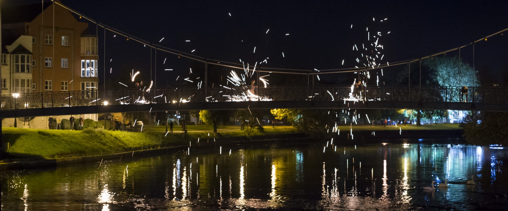 On a bridge over Exeter canal, fire spinners perform, sparks flying off into the night sky.