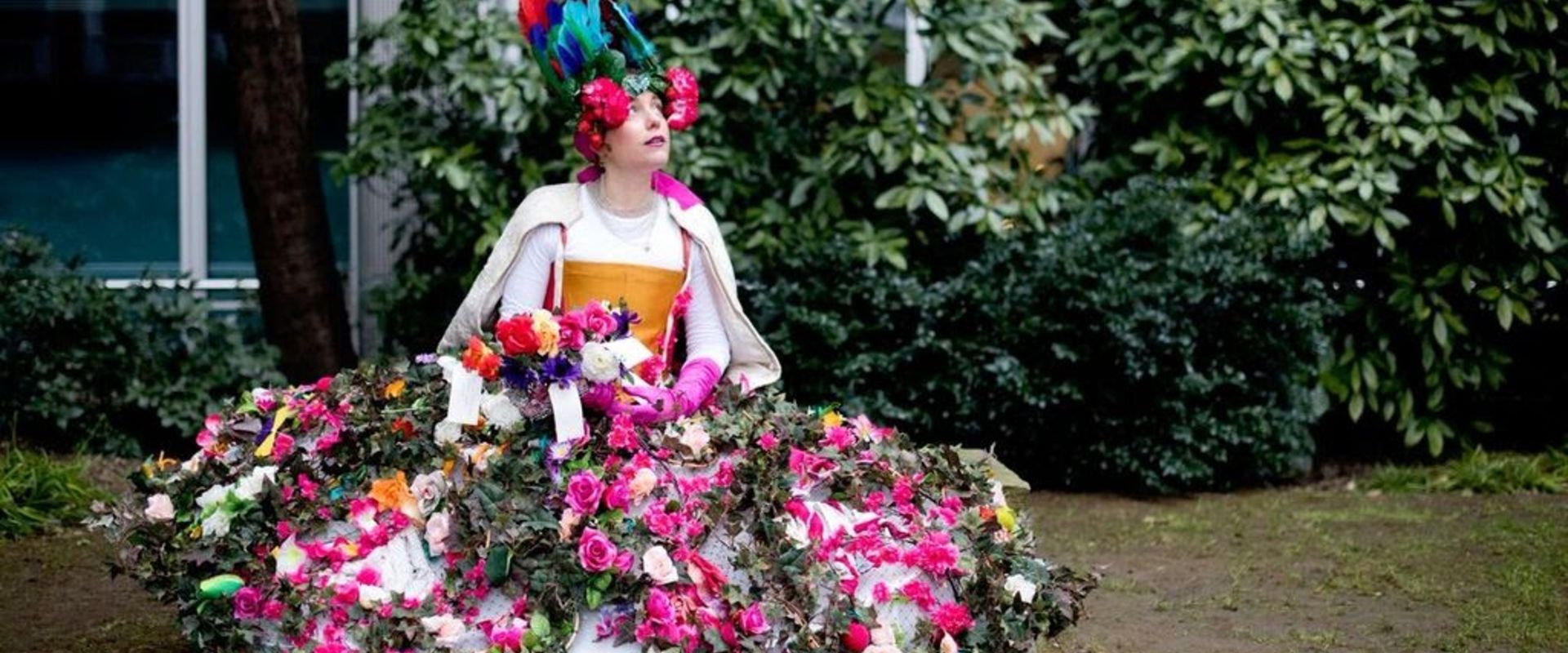 A character, dressed in a giant skirt decorated with flowers of all colours, and an equally floral headdress.