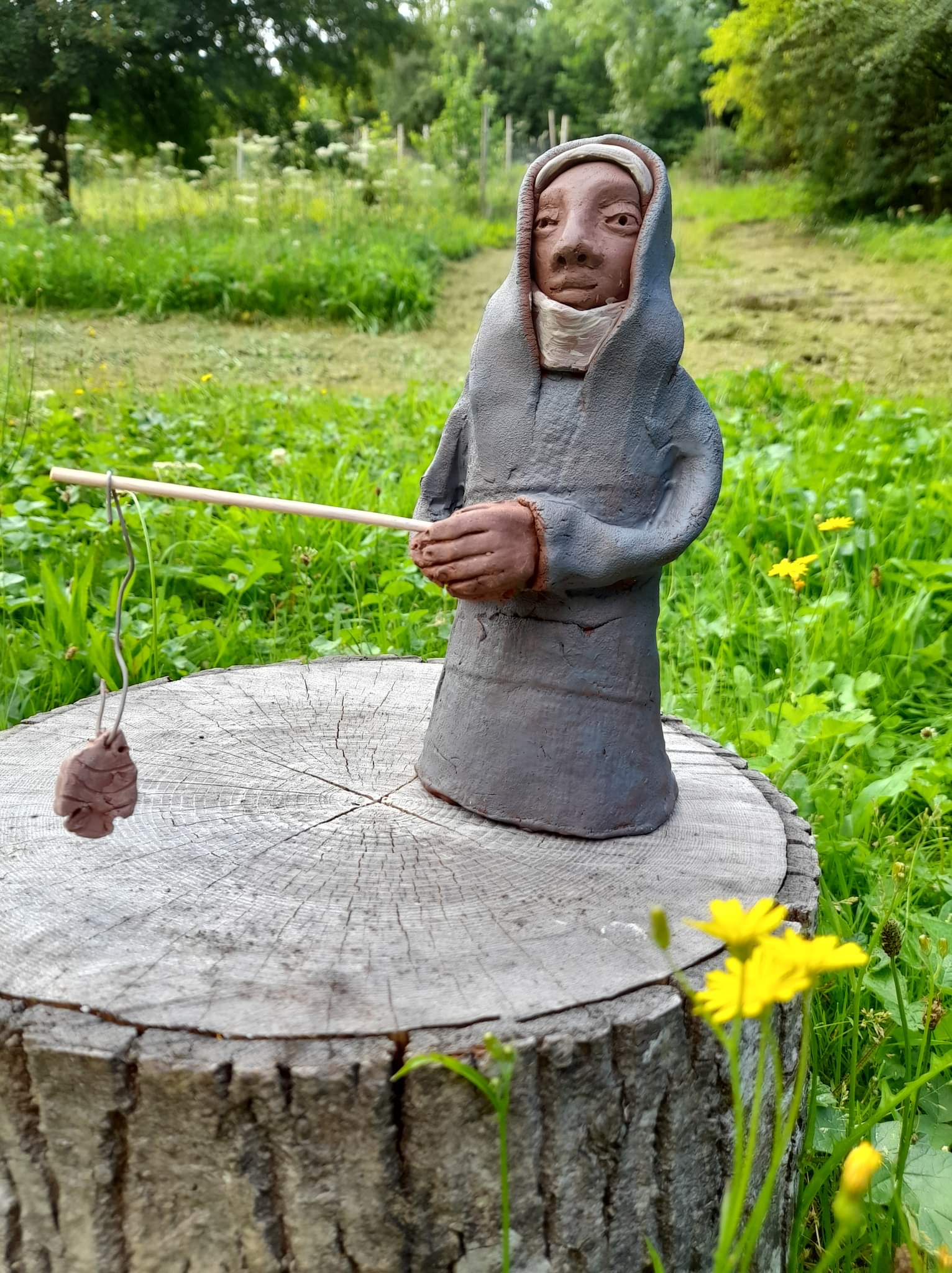 Handmade clay nun fishing atop a log.